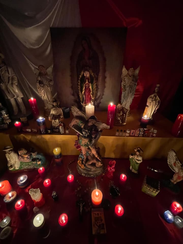 Mi altar de la Virgen de Guadalupe con San Miguel, santos y veladoras rojas encendidas.